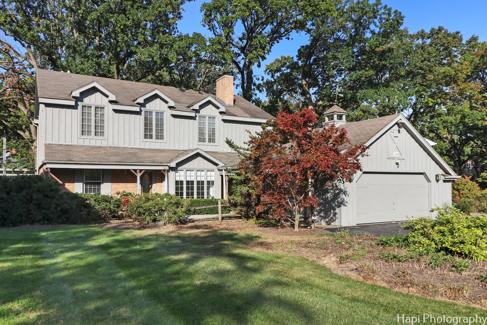 a view of a white house next to a yard with plants and large trees