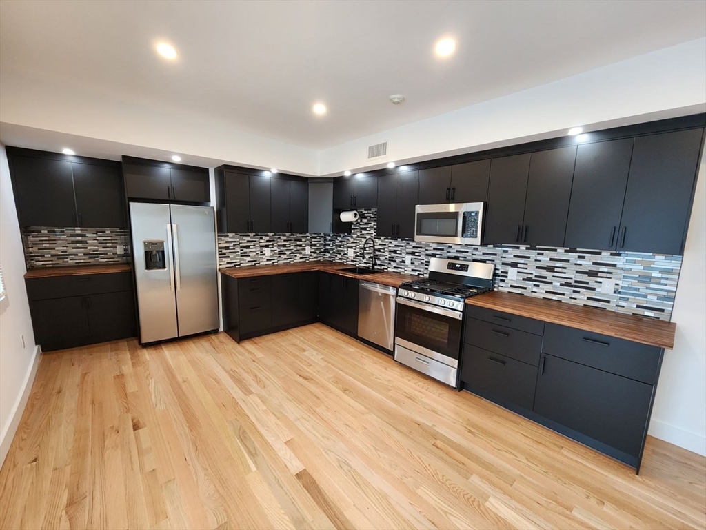 a large kitchen with stainless steel appliances kitchen island granite countertop a stove and a refrigerator