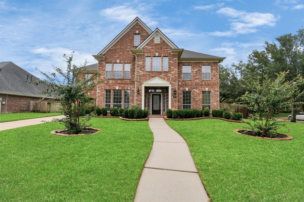 Charming two-story corner lot home with a covered porch, manicured lawn, and mature trees. Featuring a mix of brick and modern accents, large windows, and a curved driveway leading to a detached garage.