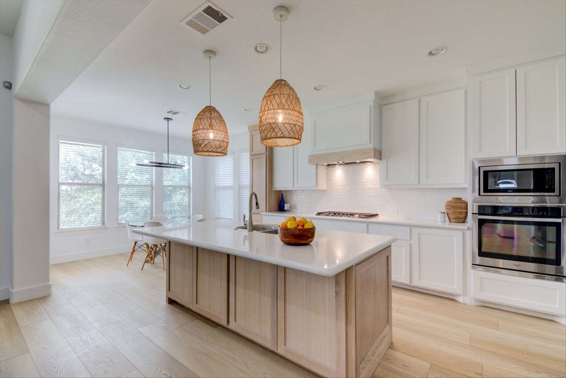 This kitchen features extra-large white oak custom cabinets, rolling organizational drawers with outlets, Serena and Lily accent lights, and wiring for under-cabinet lighting.