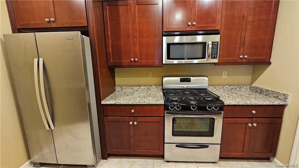 Kitchen featuring light tile patterned flooring, stainless steel appliances, and light stone countertops