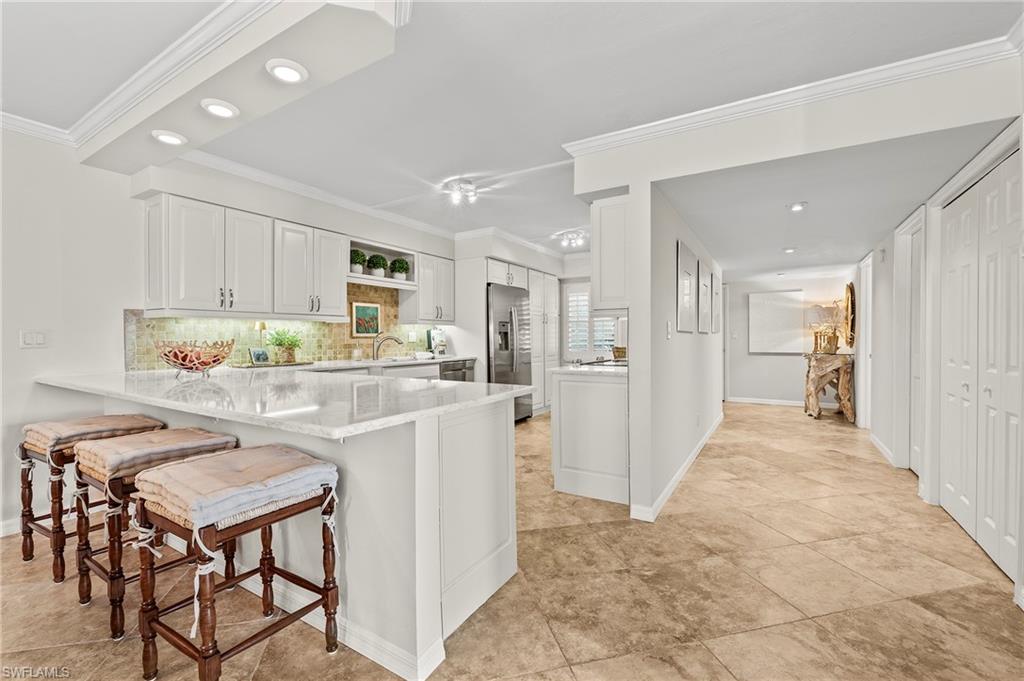 Kitchen with kitchen peninsula, a kitchen breakfast bar, crown molding, white cabinetry, and stainless steel fridge