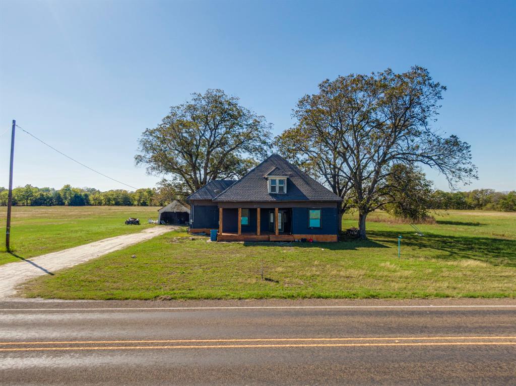 View of front of house with a front yard, a rural view, and covered porch