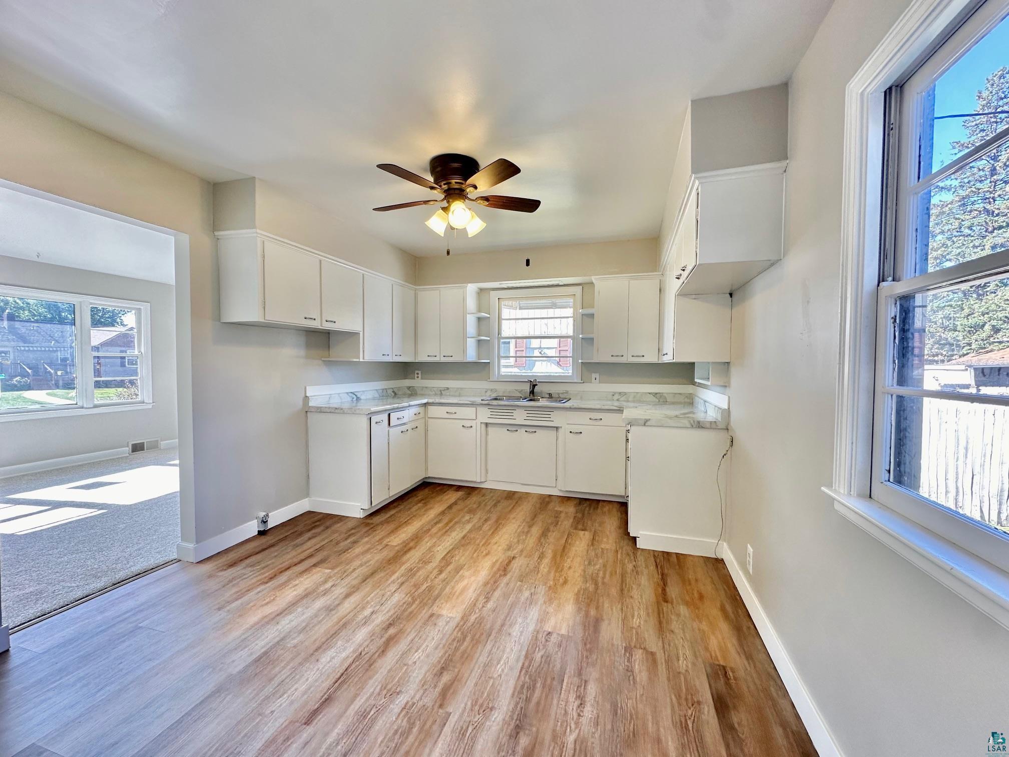 Kitchen with light hardwood / wood-style floors, white cabinets, sink, and ceiling fan