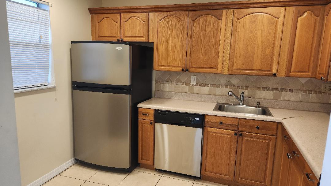 a utility room with stainless steel appliances granite countertop a refrigerator and a sink