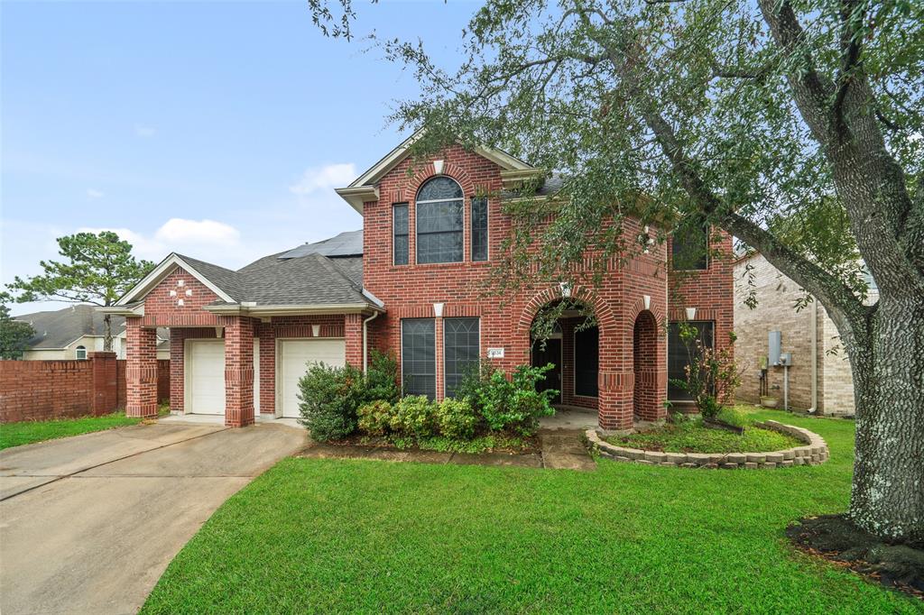 This charming two-story brick home features a welcoming front entrance with archways, a well-maintained lawn, a two-car garage, and mature trees providing shade and curb appeal.