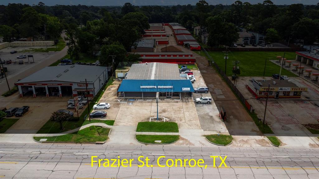 This aerial photo showcases a commercial area on Frazier St. in Conroe, TX, with a mix of businesses including a car wash, storage facilities, and eateries, set amidst a backdrop of trees and a residential neighborhood.