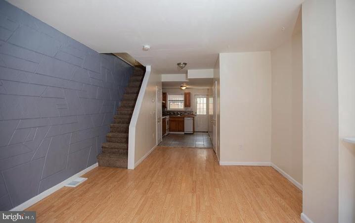 a view of a hallway to an empty room with wooden floor and a kitchen