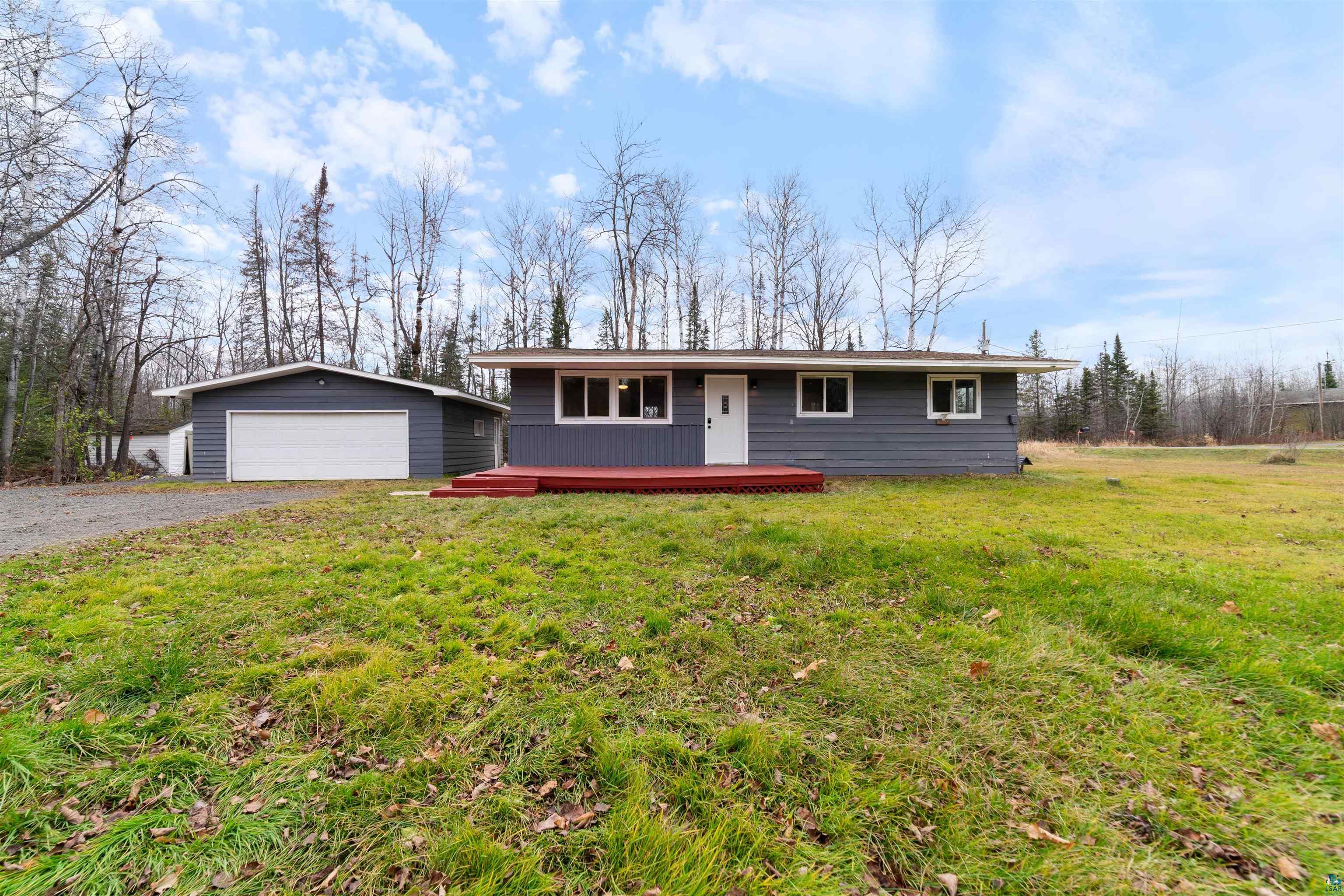 Ranch-style house with a front yard, a garage, an outdoor structure, and a deck