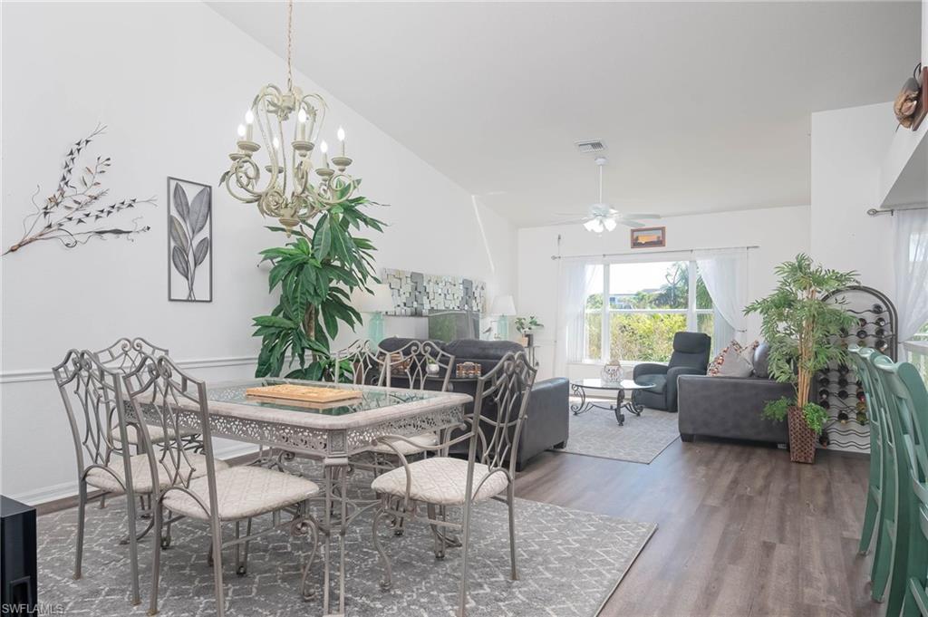 Dining room featuring dark wood-type flooring, vaulted ceiling, and ceiling fan with notable chandelier