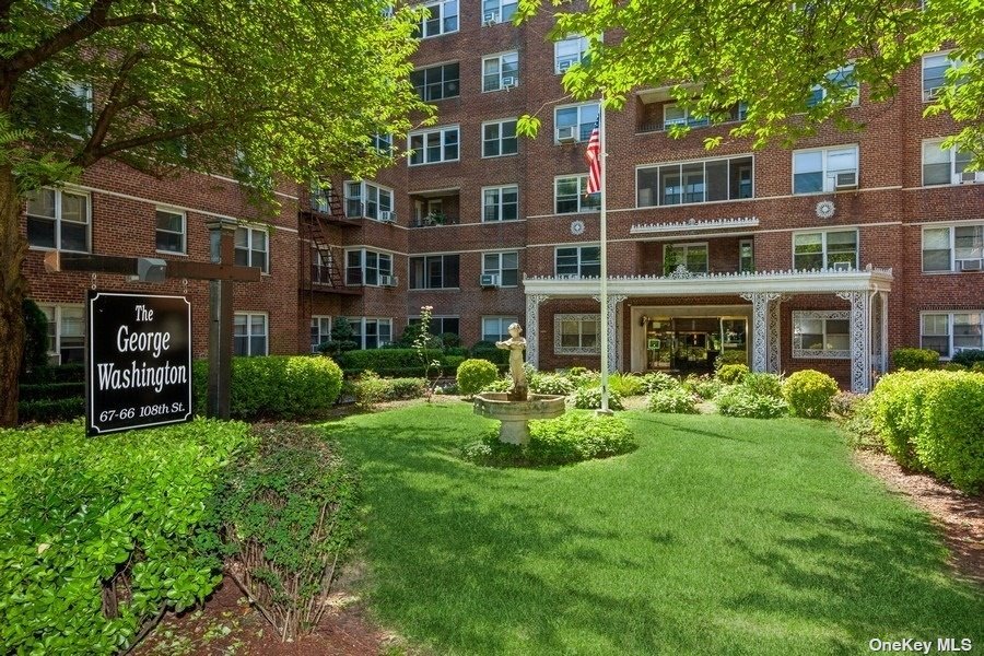 a view of a brick building next to a big yard and large trees