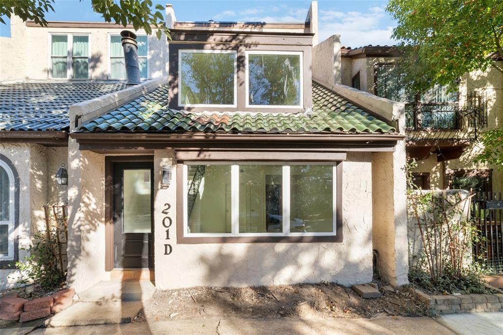 Charming townhouse with a textured stucco exterior and green tiled roof. It features new low-e windows and a cozy entrance, offering natural light and a welcoming atmosphere.