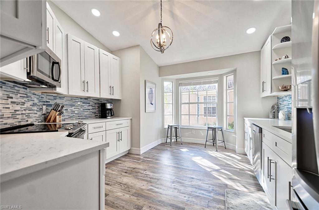 Kitchen featuring light hardwood / wood-style floors, white cabinetry, light stone countertops, lofted ceiling, and decorative light fixtures