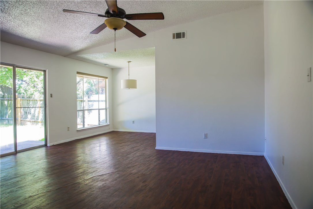 an empty room with wooden floor chandelier fan and windows