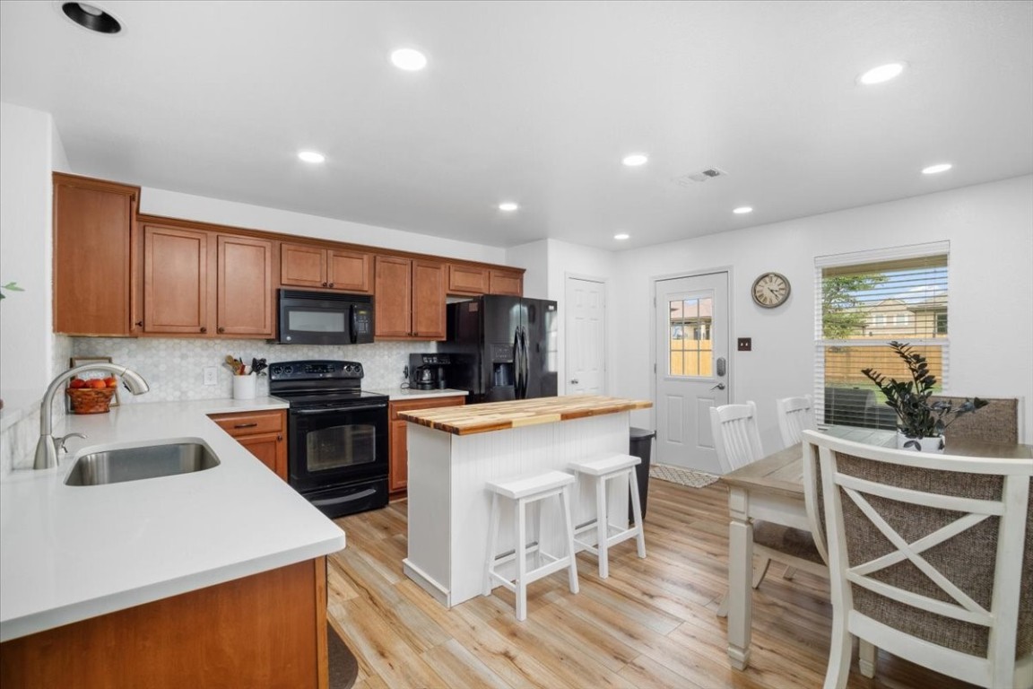 a kitchen with stainless steel appliances kitchen island granite countertop a stove top oven a sink a dining table and chairs with wooden floor