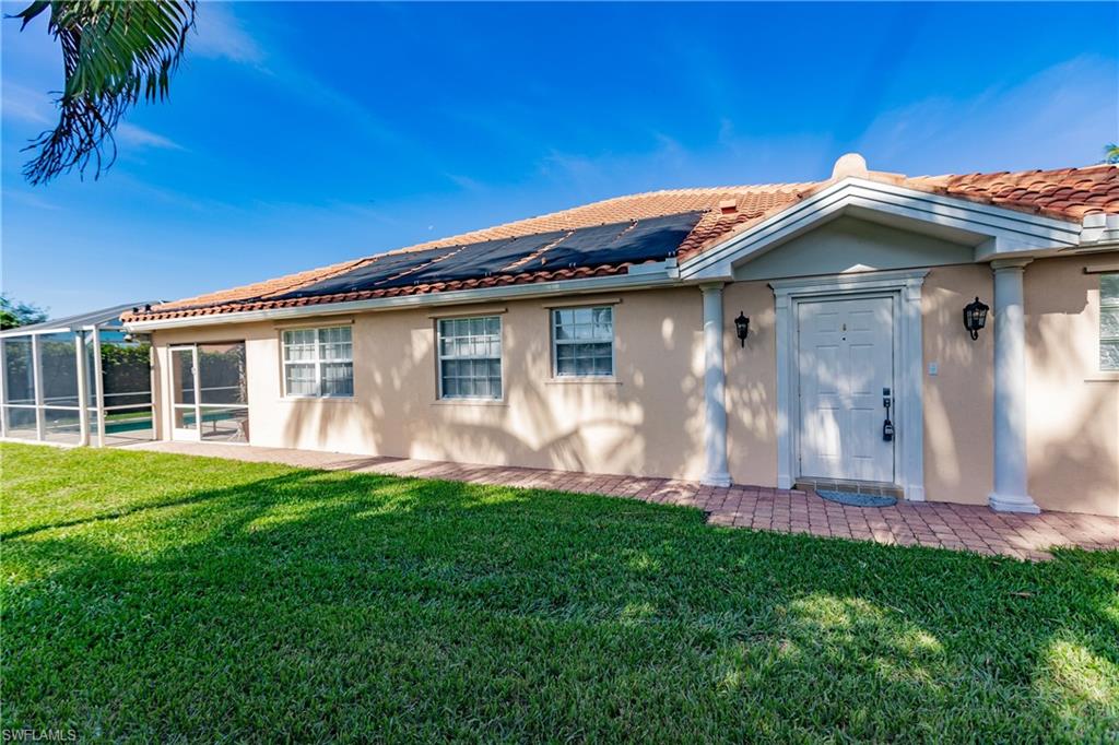 Back of property with a lawn, solar panels, and a lanai