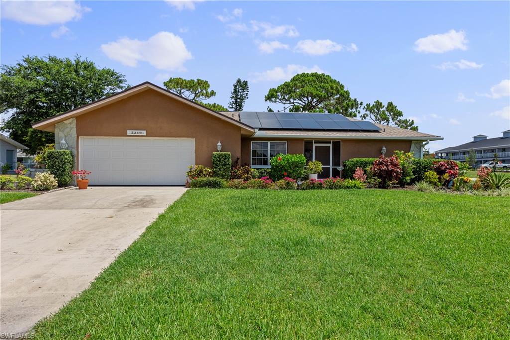 Ranch-style home with a front yard, a garage, and solar panels