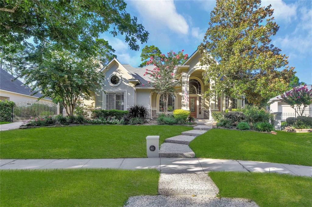 This is an elegant single-family home featuring a manicured lawn, mature trees, and a charming pathway leading to an inviting entrance with an arched doorway. The property boasts a well-maintained facade with large windows, offering a picturesque suburban living experience.