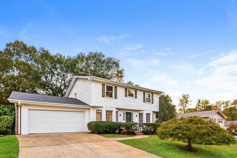 a view of a white house next to a yard with big trees