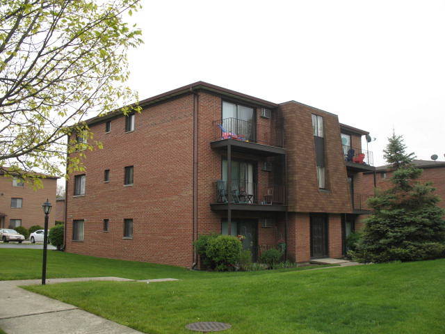 a brick house that is sitting in front of a big yard with plants and large trees