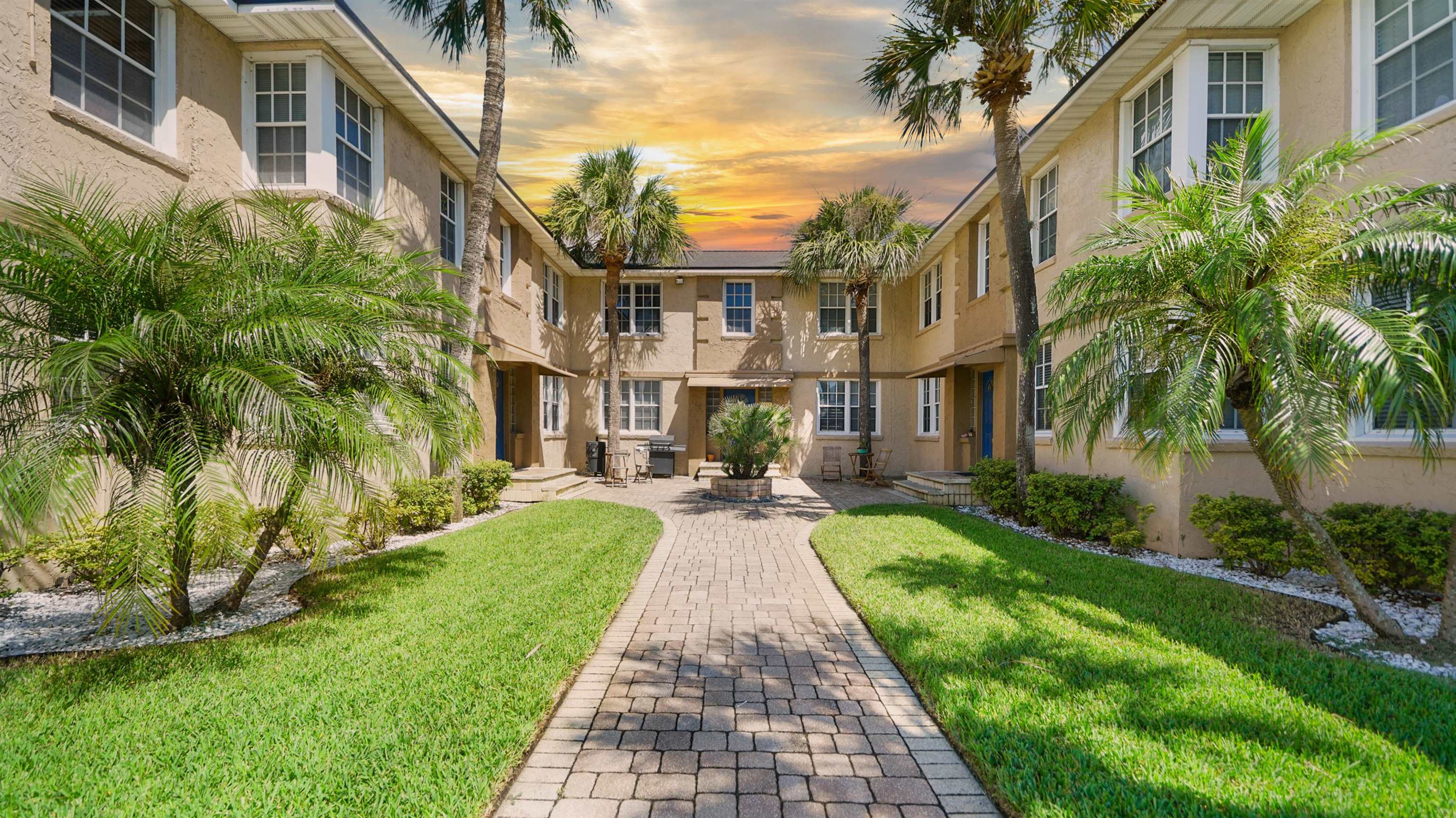 a view of a brick house with a big yard plants and palm trees