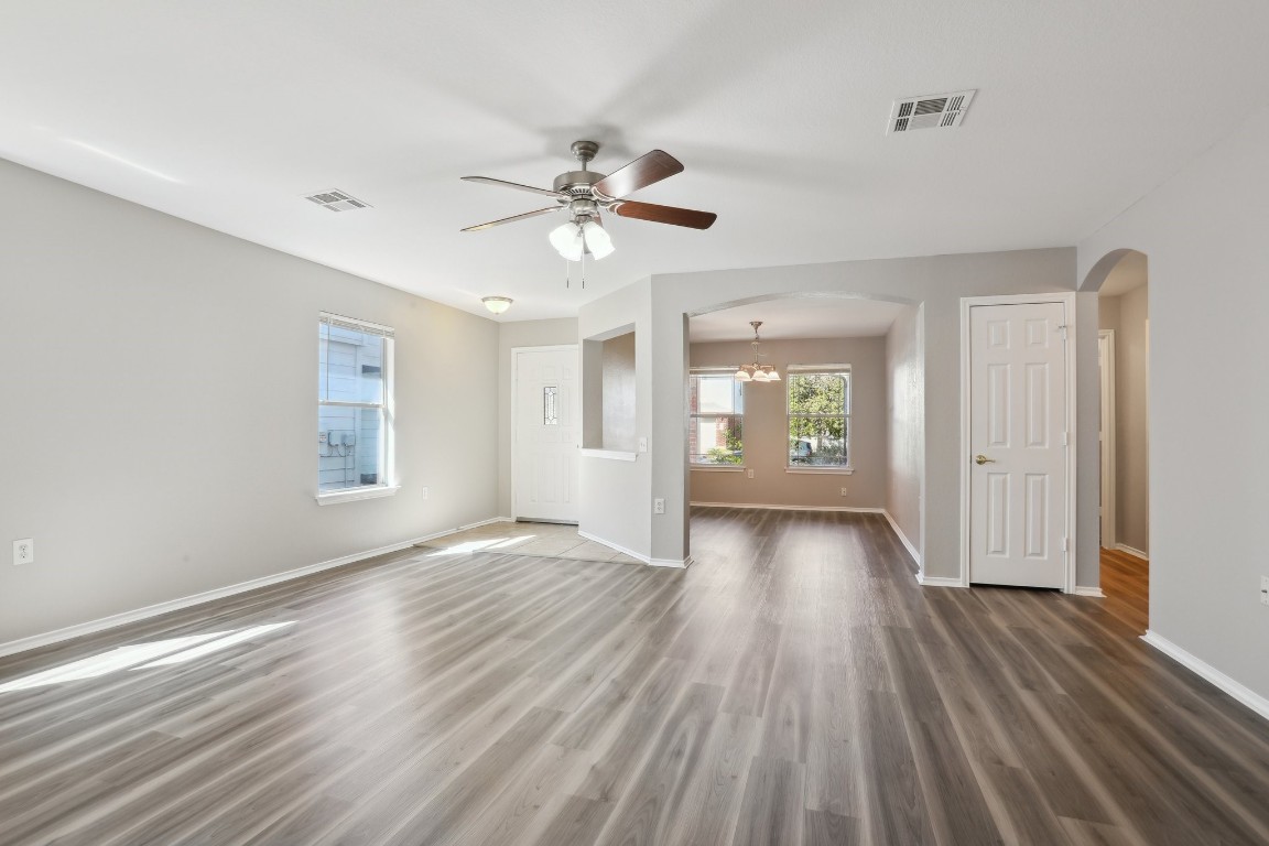 an empty room with wooden floor chandelier fan and windows