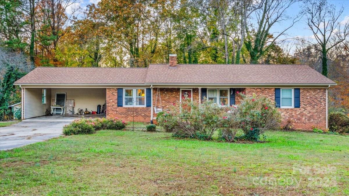 a view of a brick house with a yard plants and large tree