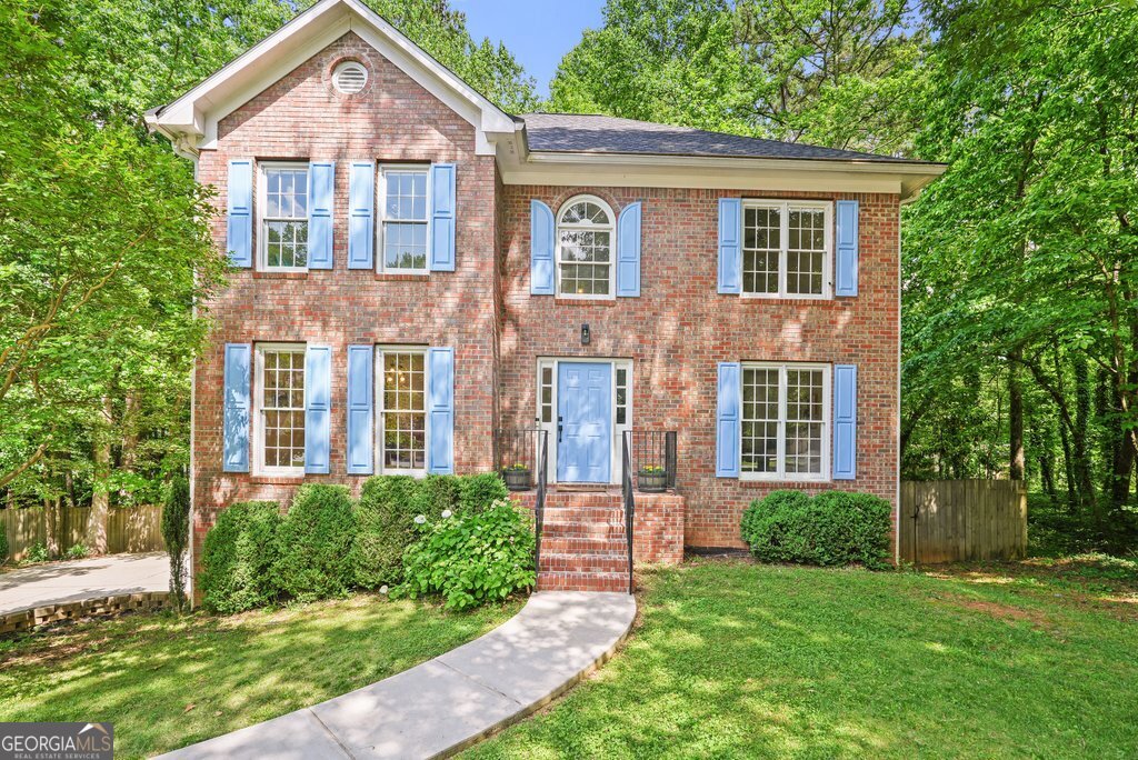 front view of a brick house with a yard and large trees