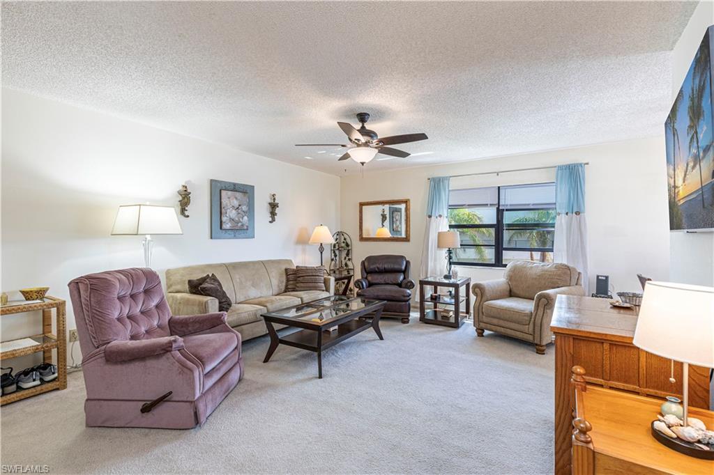 Living room with a textured ceiling, light colored carpet, and ceiling fan