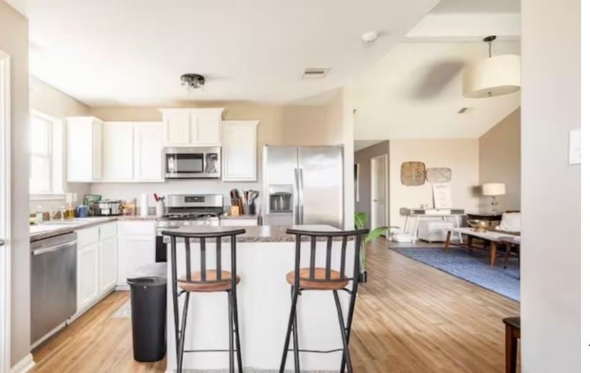 a kitchen with stainless steel appliances kitchen island granite countertop a stove top oven a sink a refrigerator a dining table and chairs with wooden floor