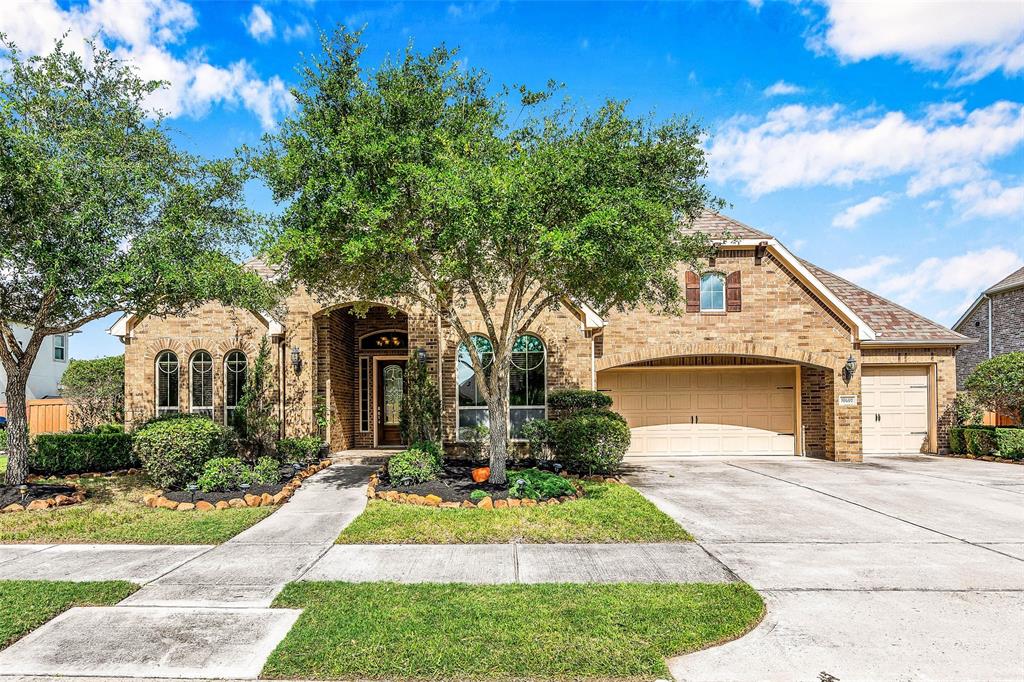 This is a single-story brick home with a well-manicured lawn, featuring a three-car garage and mature trees in the front yard, enhancing its curb appeal. 4 bedrooms + home office study + 3 Car Garage.