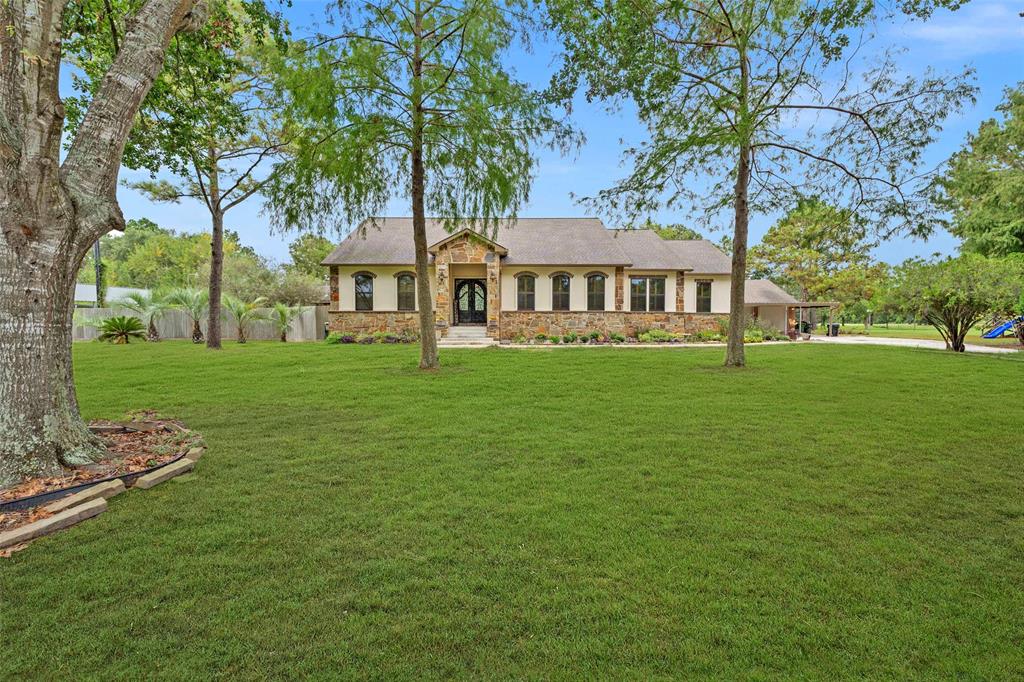 This is a single-story, traditional-style home with a well-manicured lawn, mature trees, and an attached garage. The house features a stone and stucco exterior with a welcoming entrance.