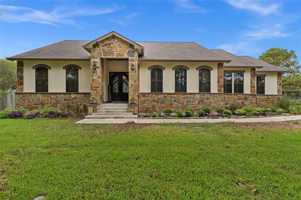 This is a single-story stone facade home with a well-manicured lawn and an elegant entryway, featuring large windows and a prominent gable over the front door.