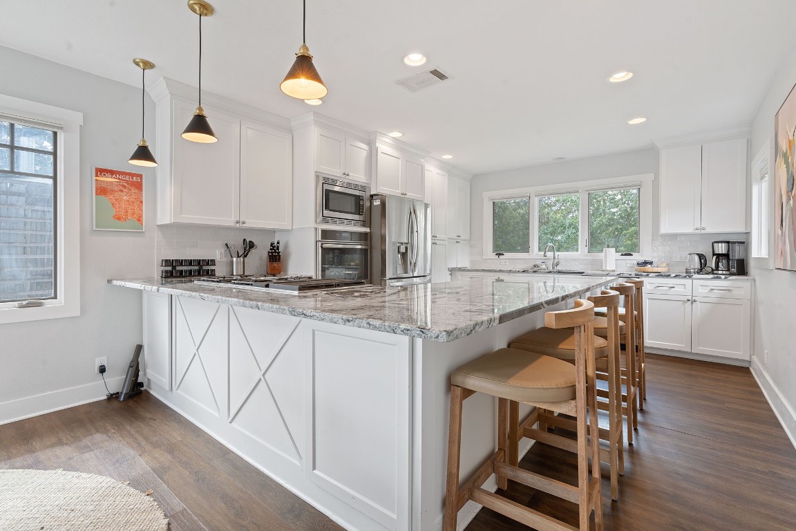 a kitchen with stainless steel appliances granite countertop a sink a stove a refrigerator cabinets and chairs