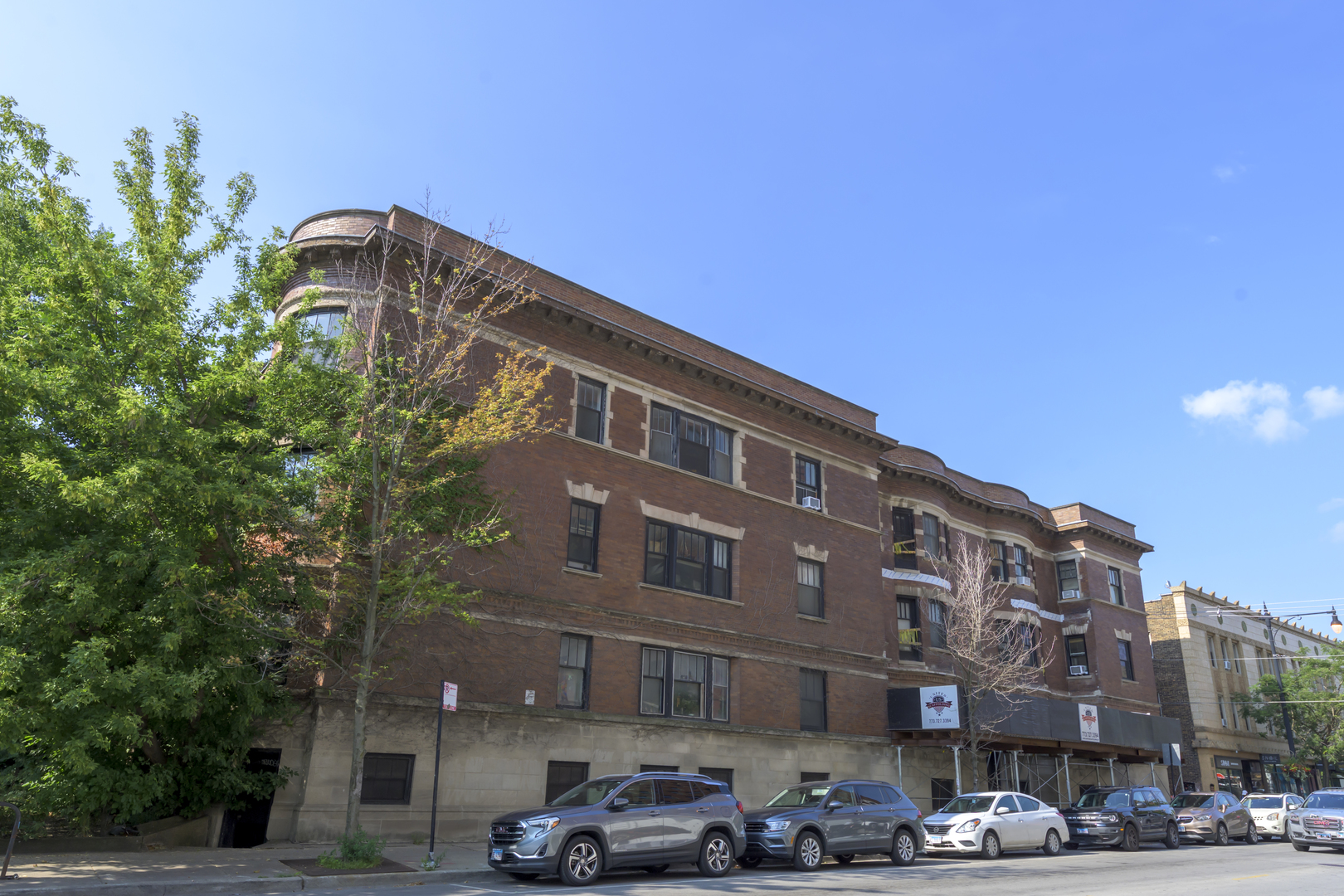 a front view of a building with lot of cars and trees