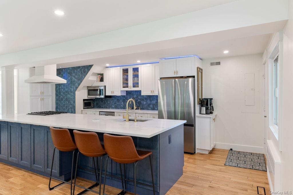 Kitchen with custom range hood, light wood-type flooring, stainless steel appliances, and sink