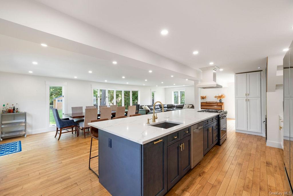 Kitchen with premium range hood, a large island with sink, sink, light hardwood / wood-style floors, and stainless steel appliances