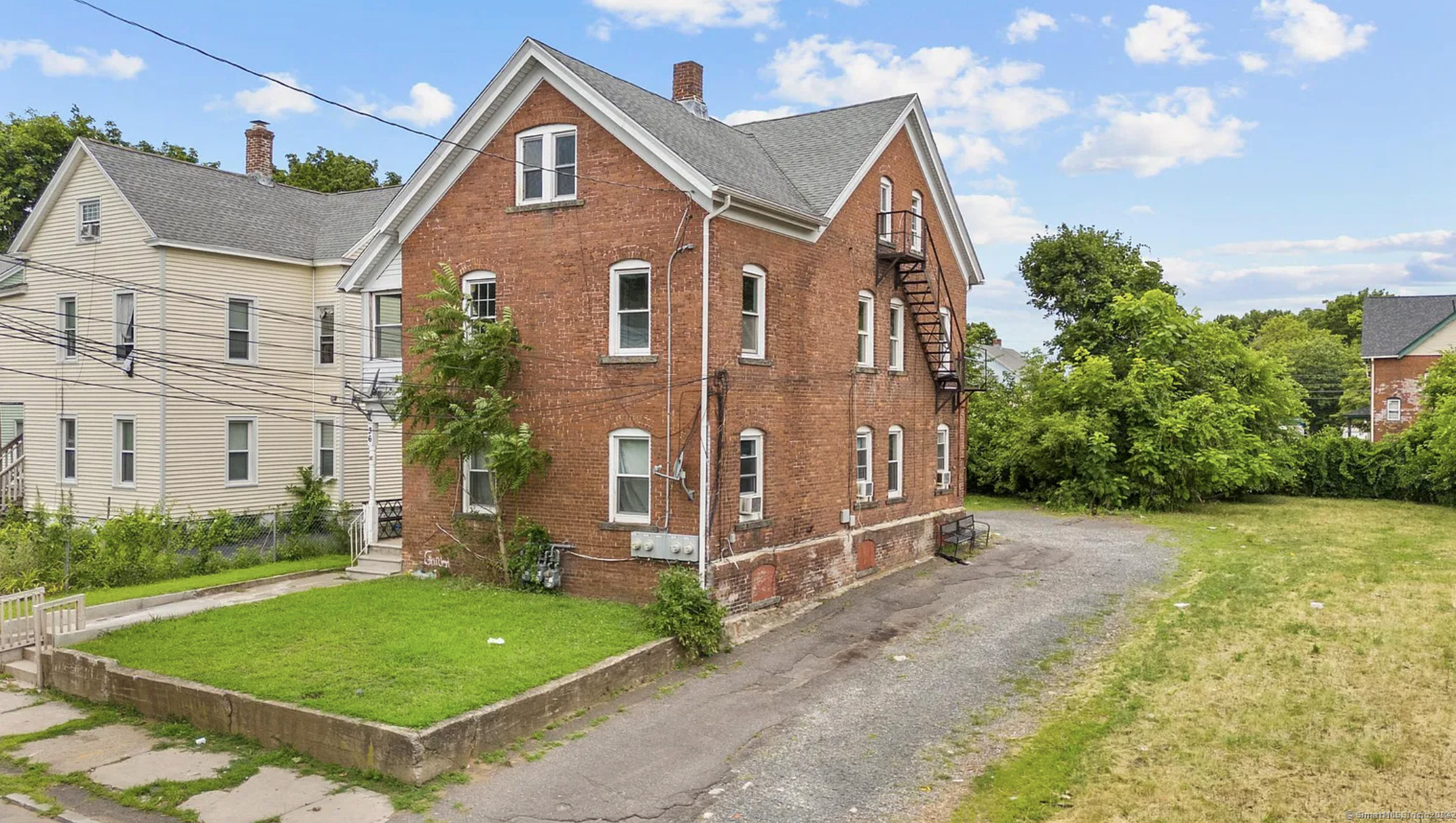 a view of a brick house with a yard plants and large tree