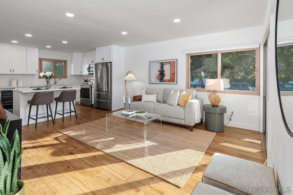 a living room with furniture a large window with kitchen view and a rug