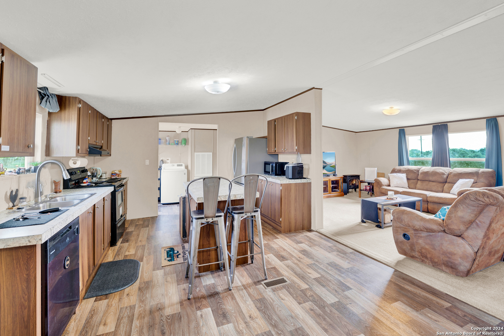 a living room with furniture a dining table wooden floor and a view of kitchen