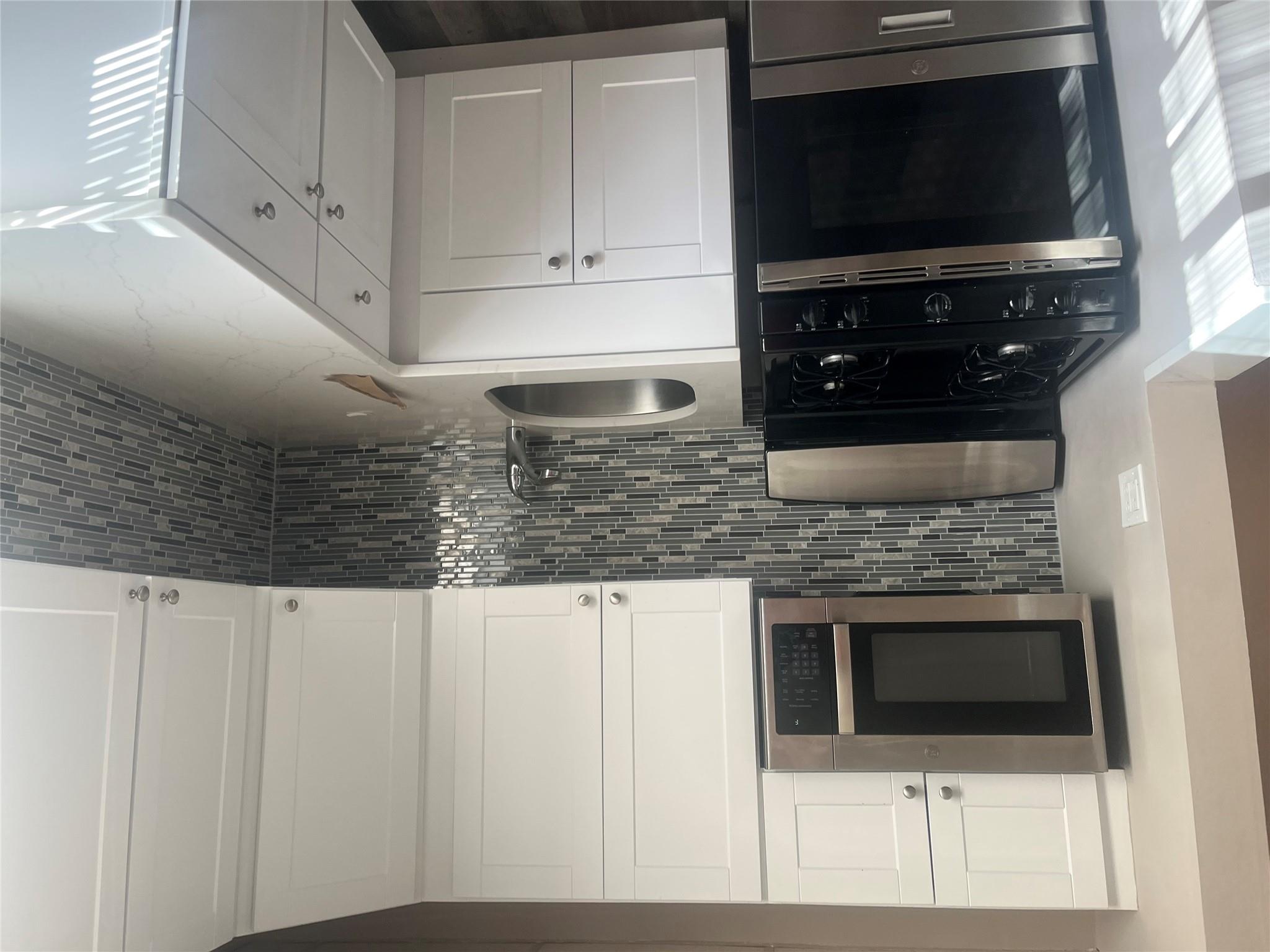 Kitchen featuring decorative backsplash, light stone countertops, sink, white cabinets, and range