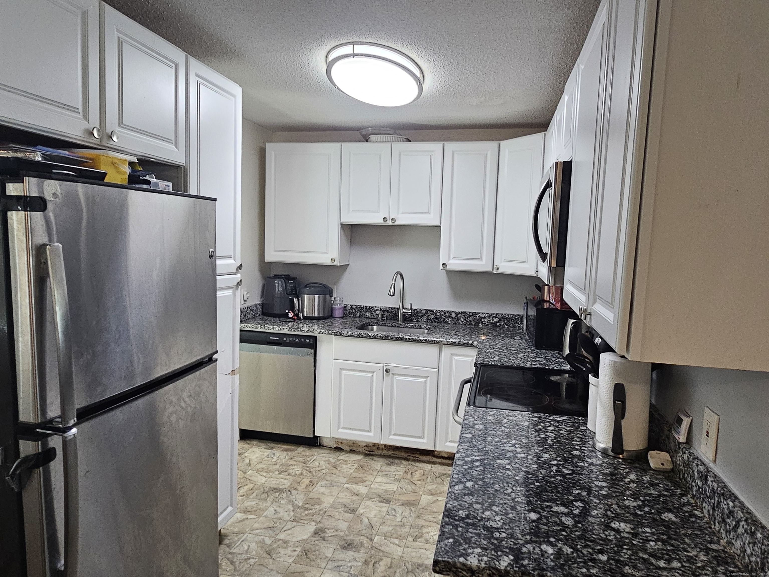 a kitchen with granite countertop a refrigerator a sink and white cabinets