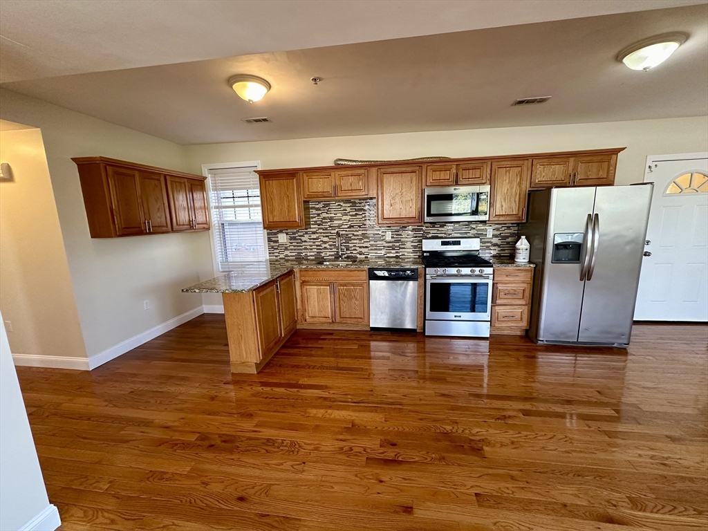 a kitchen with stainless steel appliances wooden floor and a refrigerator