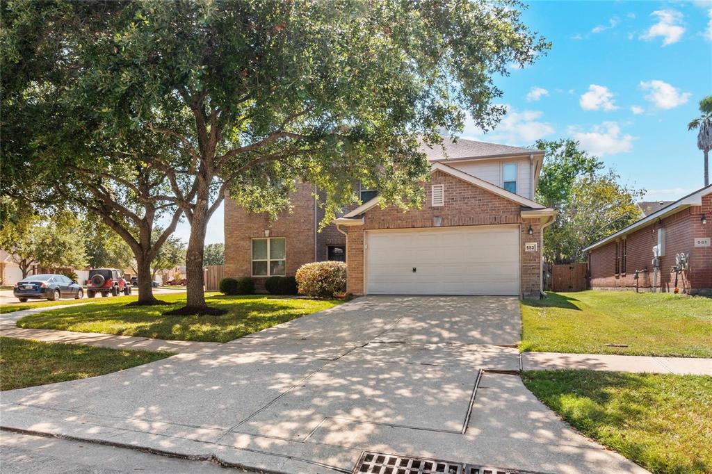 Charming two-story brick home with a spacious driveway and attached garage. The front yard features mature trees and well-maintained landscaping, creating a welcoming atmosphere. Located on a quiet street with ample sidewalk space.