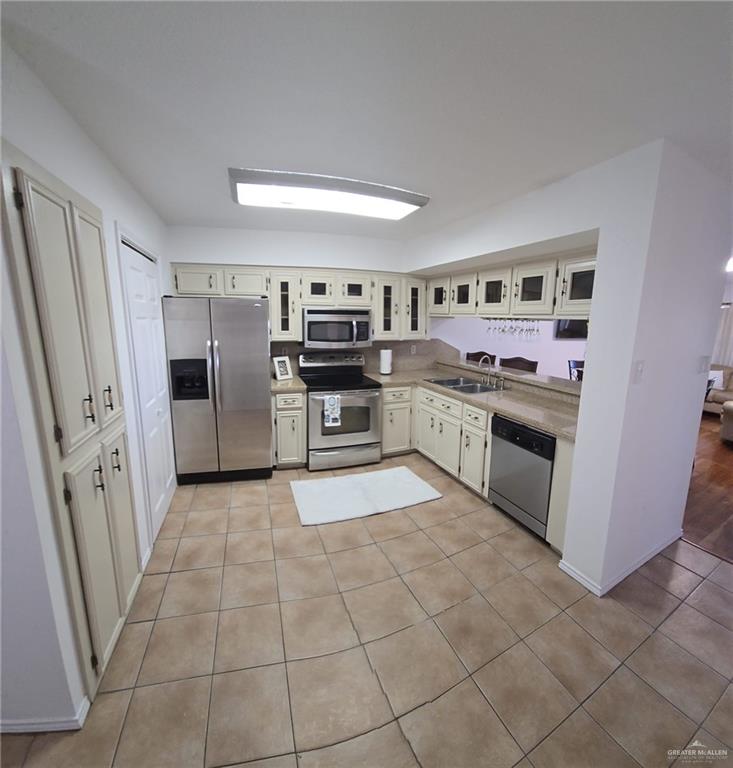 Kitchen featuring light tile patterned floors, appliances with stainless steel finishes, sink, and cream cabinets