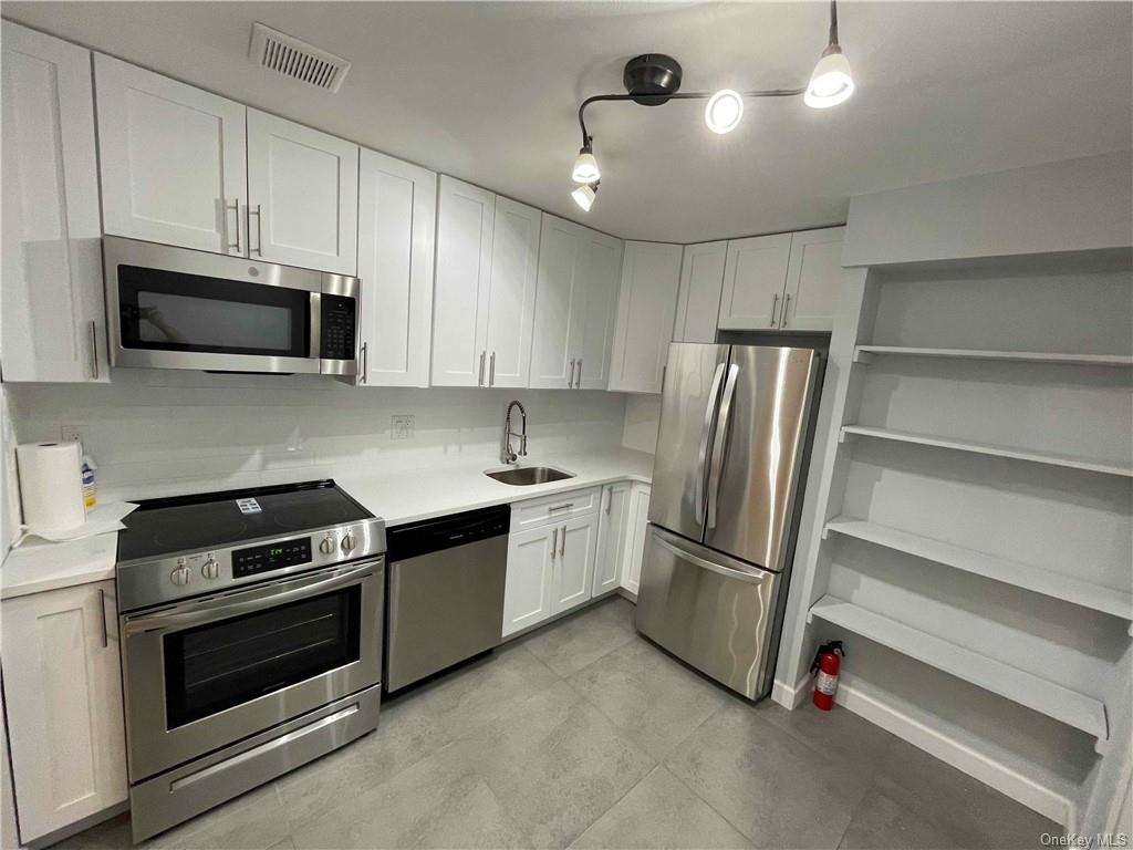 Kitchen featuring stainless steel appliances, sink, decorative light fixtures, and white cabinets