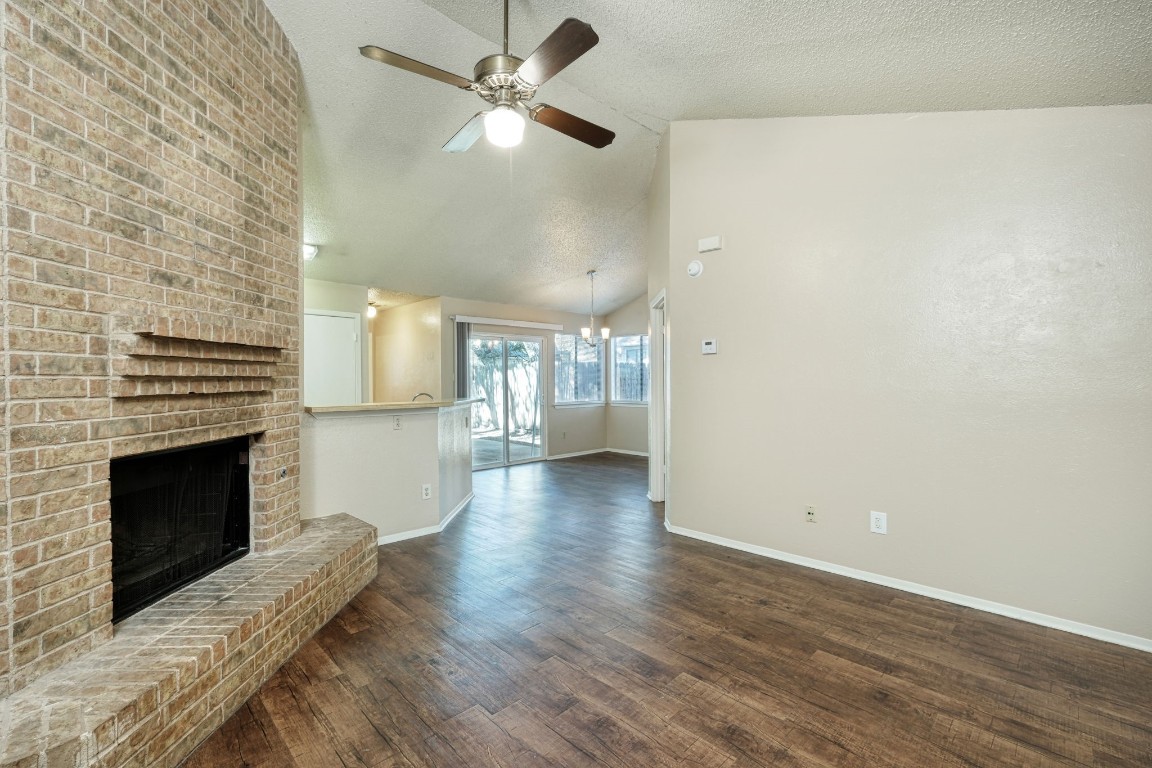 an empty room with wooden floor fireplace and a kitchen view