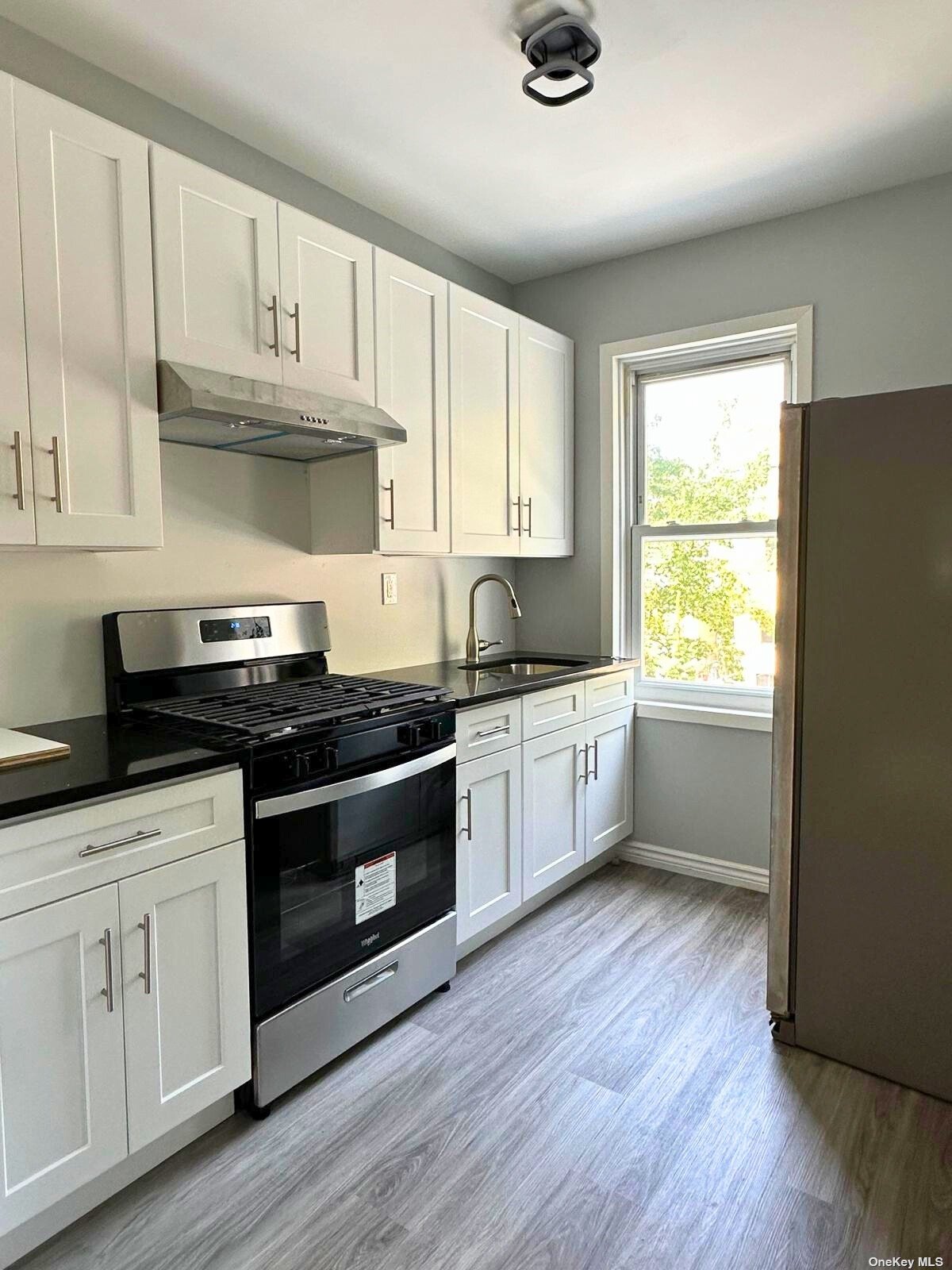 a kitchen with granite countertop wooden floors stainless steel appliances and window