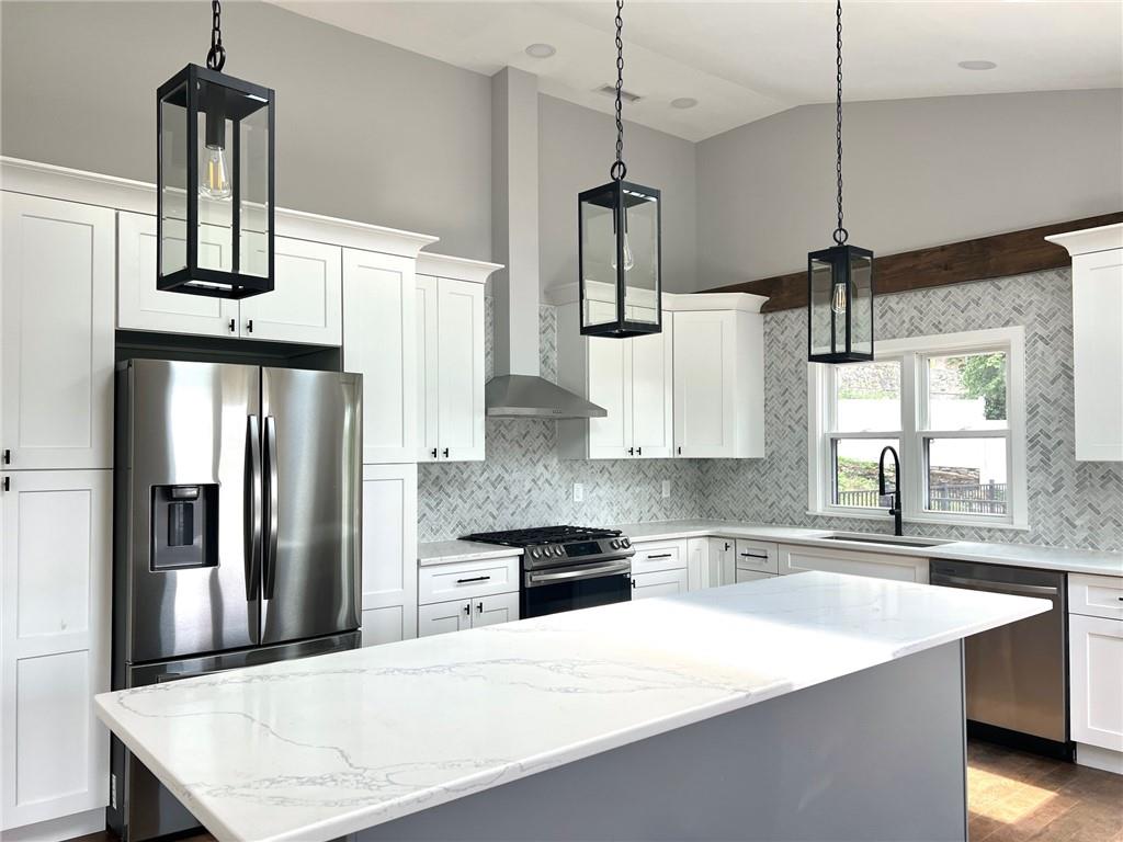 Kitchen with appliances with stainless steel finishes, lofted ceiling, backsplash, white cabinets, and sink