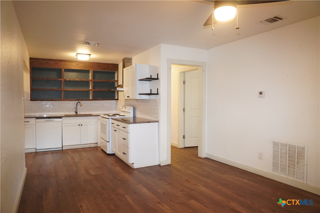 a large white kitchen with a sink dishwasher a stove and a refrigerator with wooden floor